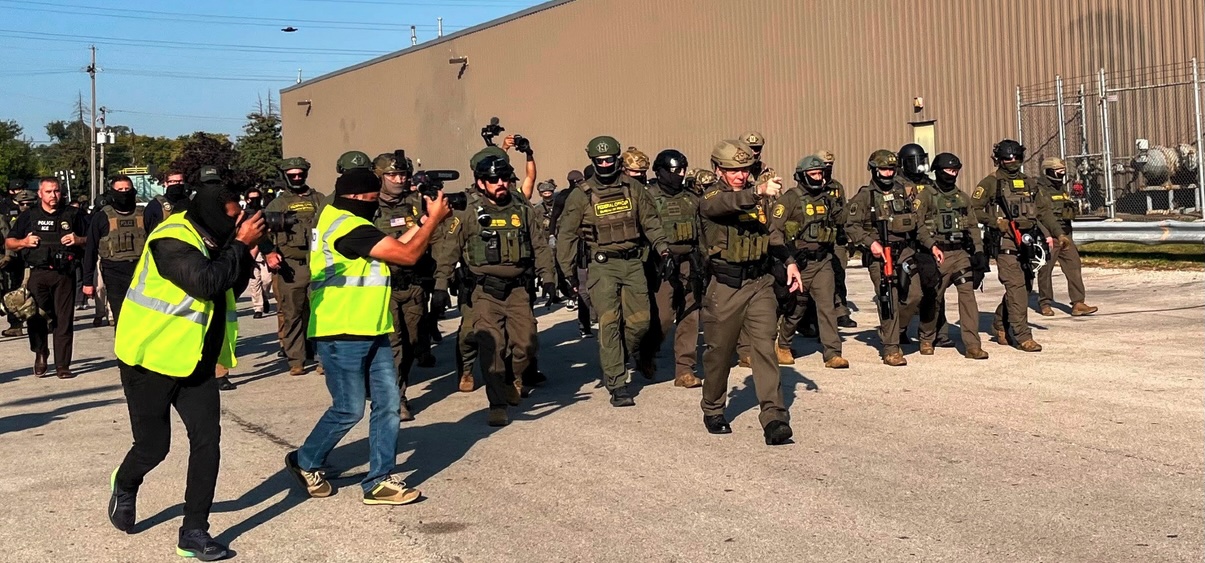 U.S. Border Patrol Sector Chief Greg Bovino, flanked by DHS cameramen and drones, starts to march into a crowd of peacful protesters on Oct 3 2025 at the Broadview ICE facility. Photo by Kelly Hayes